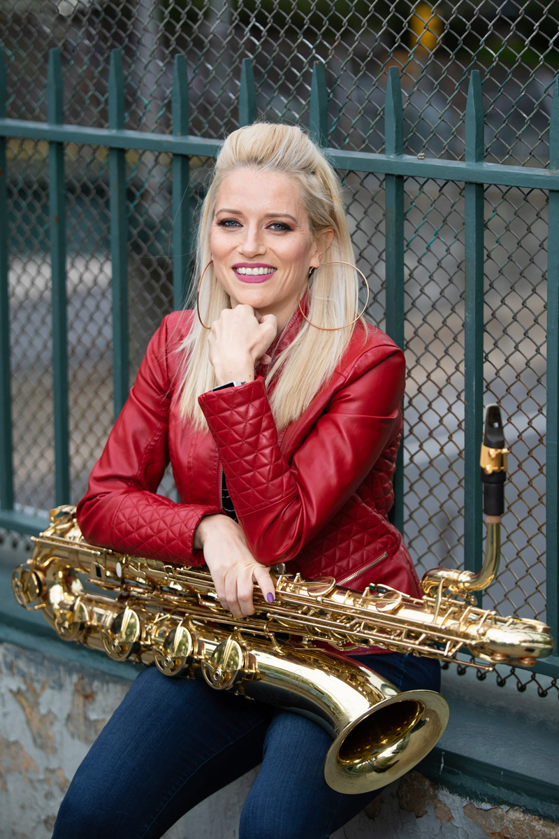 A woman in a red leather jacket smiles as she holds a saxophone