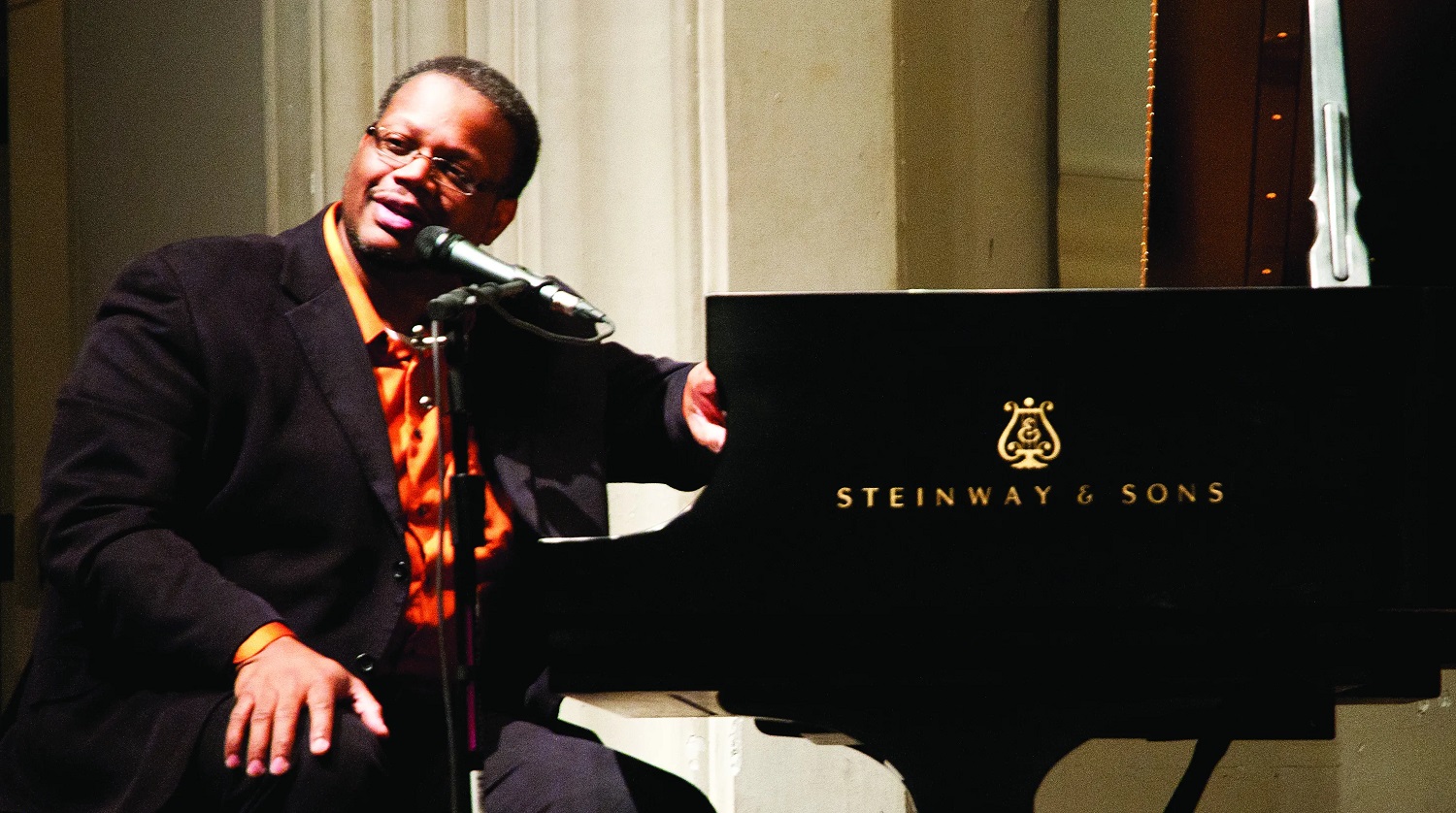 Reginald "Reggie" Thomas sits at a Steinway piano speaking into a microphone