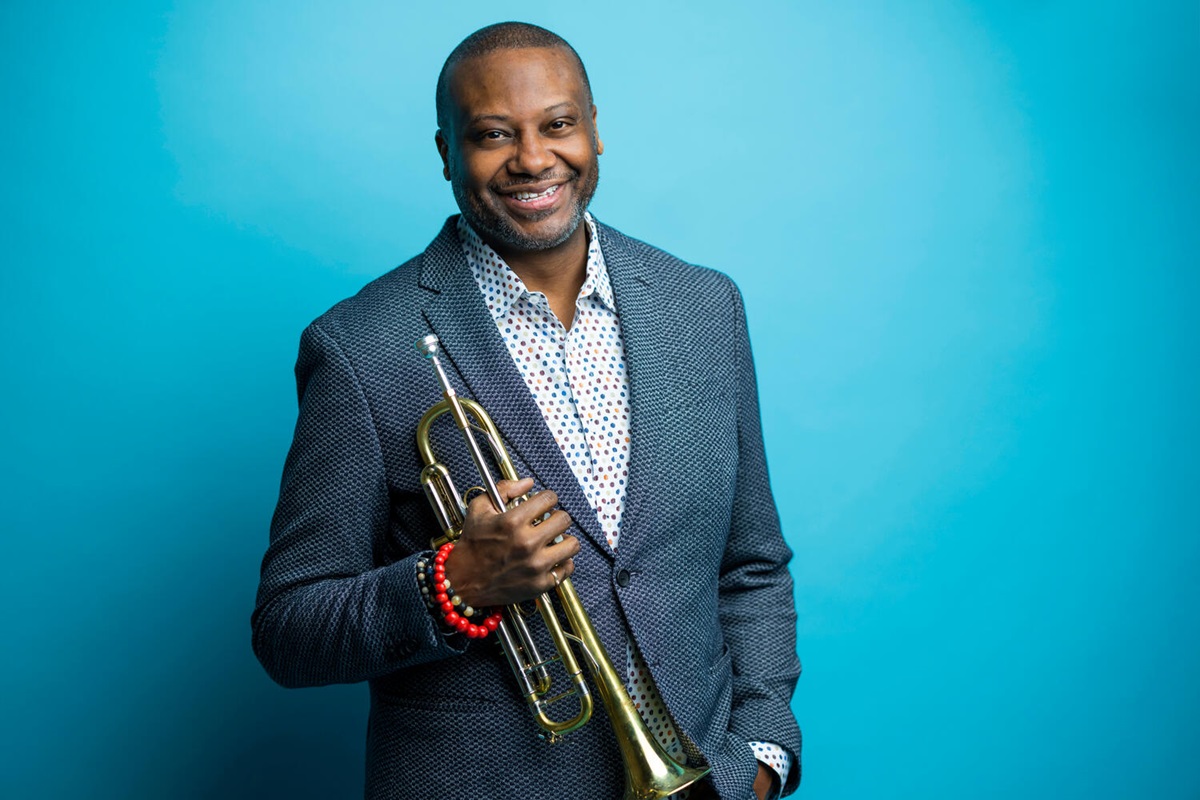 Smiling Sean Jones with trumpet against a light blue background